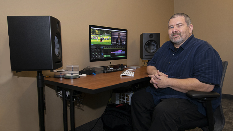 Mark Slusher sits at his computer desk, with video editing software opened.